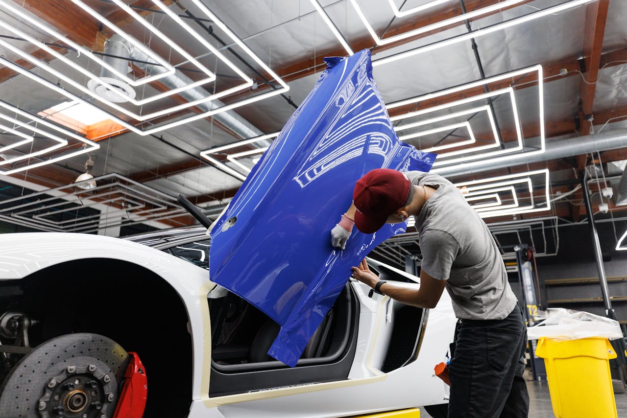 Auto mechanic applying blue vinyl wrap to a car door in a modern garage.